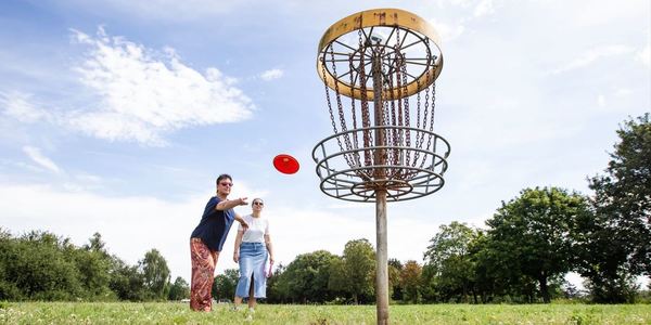 Twee volwassenen spelen disc golf in de groene omgeving van Fort 3